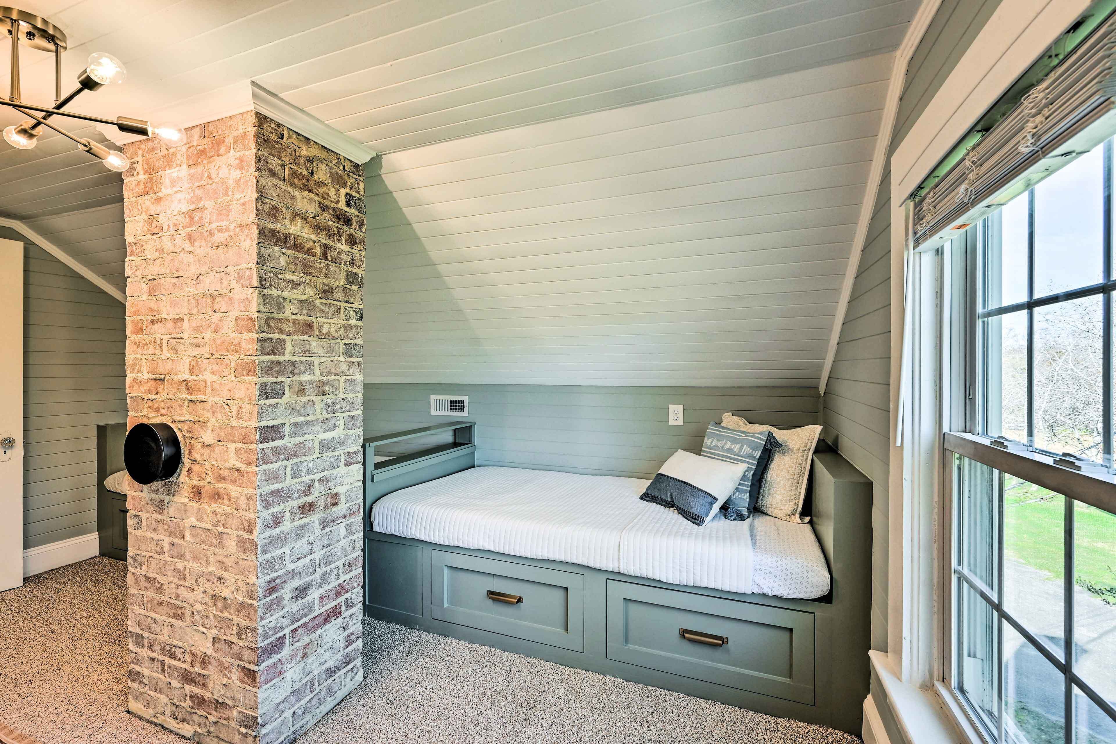 Una camera da letto con soffitto spiovente, parete decorata con mattoni, letto con cassetti contenitori e finestra vista esterna.
