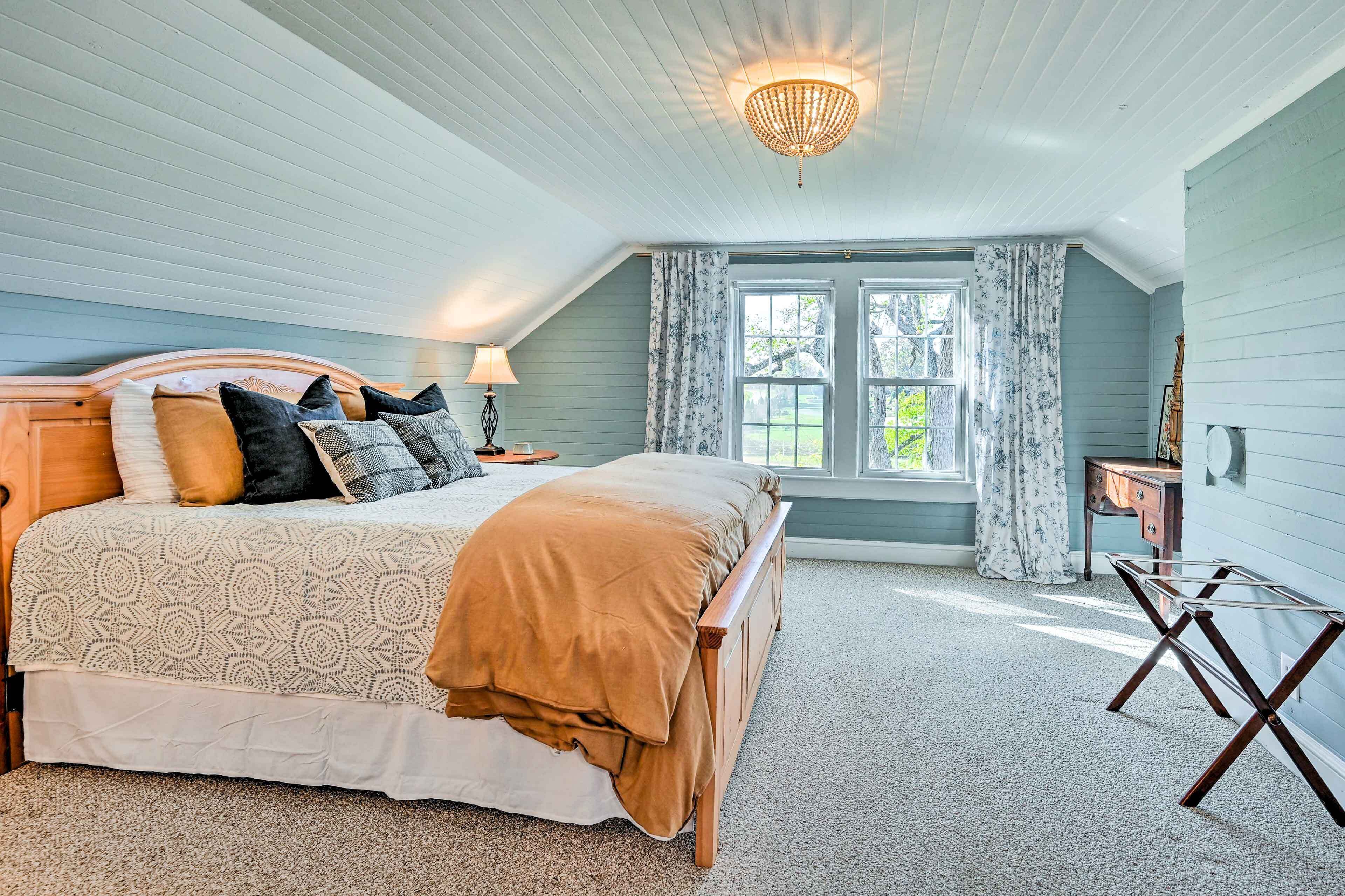 A bedroom with a large bed, a wooden nightstand, a desk, and a window with curtains.