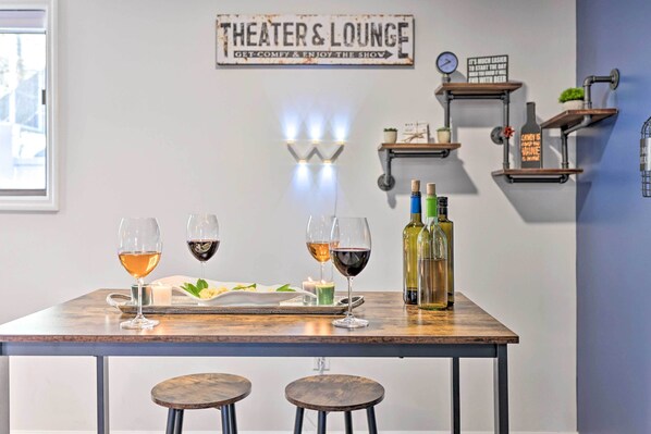 Um quarto acolhedor com uma mesa posta para refeições, dois banquinhos e uma placa com a inscrição “THEATER & LOUNGE”.