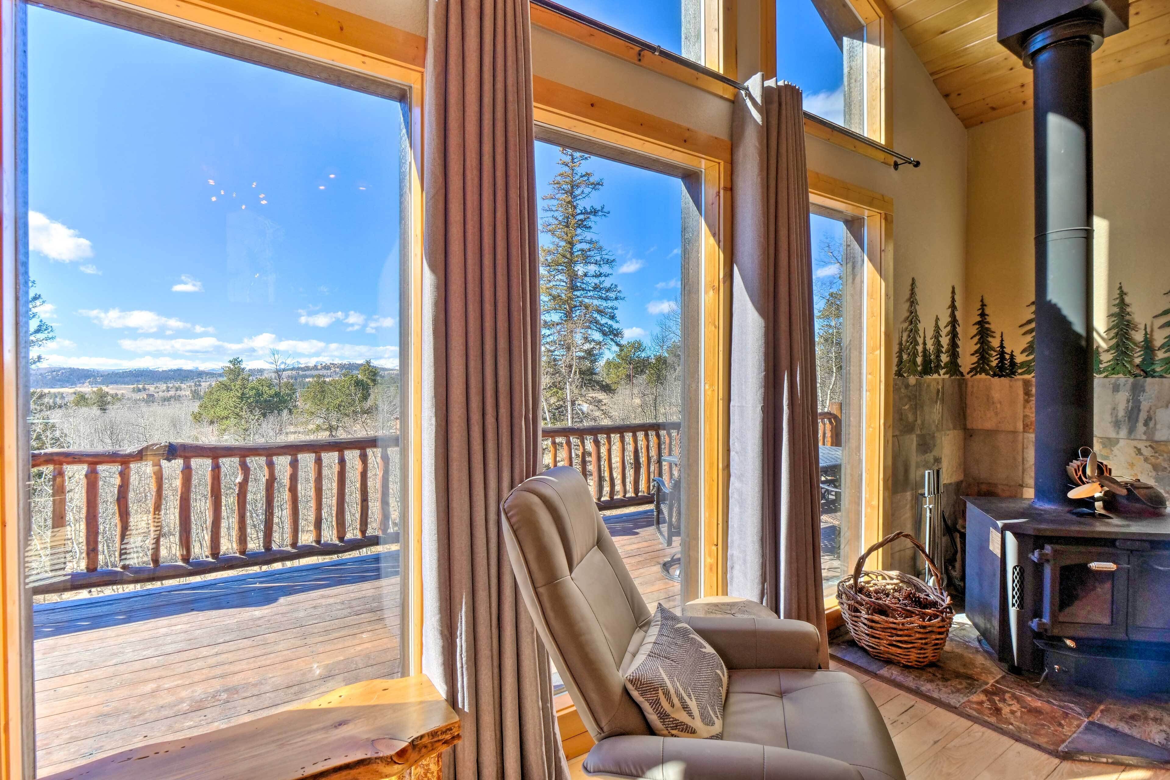 A cozy room with a large window, a comfortable chair, a fireplace, and a deck outside.