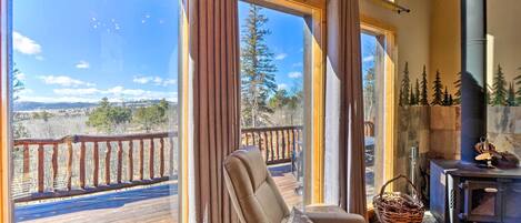 A cozy room with a large window, a comfortable chair, a fireplace, and a deck outside.