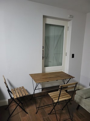 A compact room with a wooden table and two chairs, a white door with a frosted glass panel, and a grey sofa. - Studio close to airport, mall, beach, museum and much more (Bradenton)