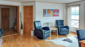 A spacious living room with wooden flooring, two leather armchairs, a small table, and a large window with a view.