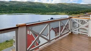 A wooden deck with a metal railing overlooking a lake and green hills.