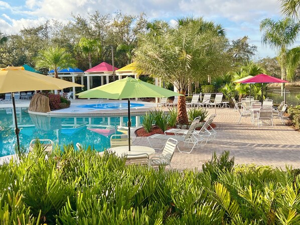 A pool area with lounge chairs and umbrellas, surrounded by palm trees and a clear sky. - 2-102 Legacy Dunes, Lake Views, Heated Pool, Free Wifi and Parking (Kissimmee)