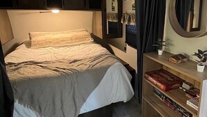 A bedroom with a bed, a bedside table with a lamp, a mirror, and a shelf with books and a plant. - Quiet, majestic views of the Shire in a cozy glamping set up!  (Brush Prairie)
