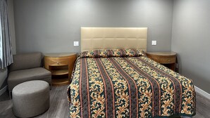 A bedroom with a bed, two nightstands, a round ottoman, and a grey couch. - Stay Inn Motel (Harbor City)