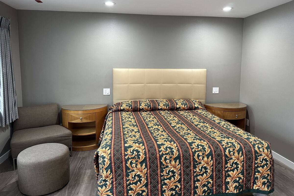 A bedroom with a bed, two nightstands, a round ottoman, and a grey couch.