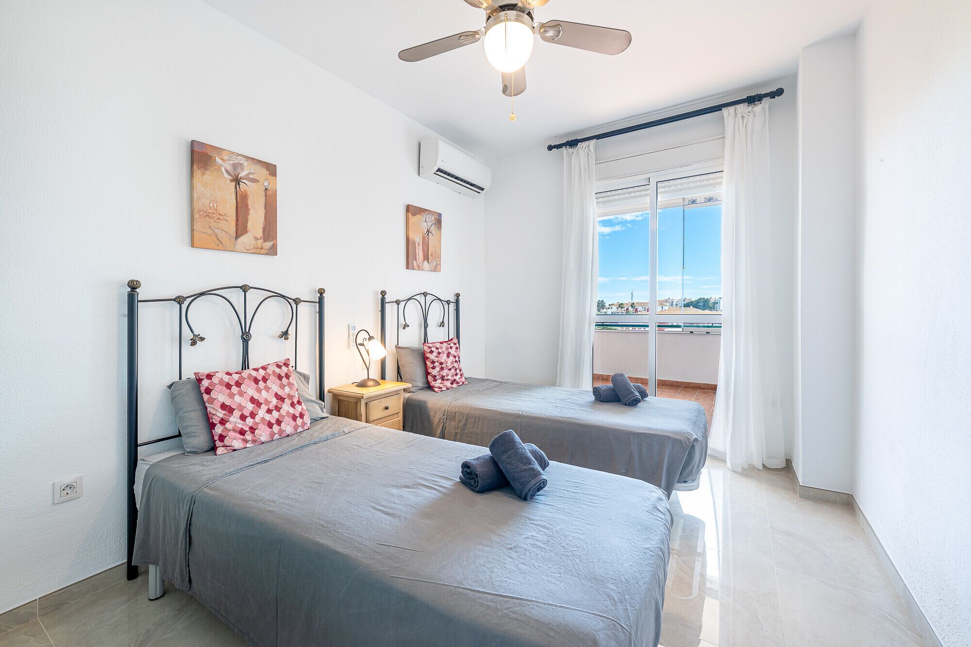 A hotel room with two beds, a ceiling fan, and a large window offering a view of the city.
