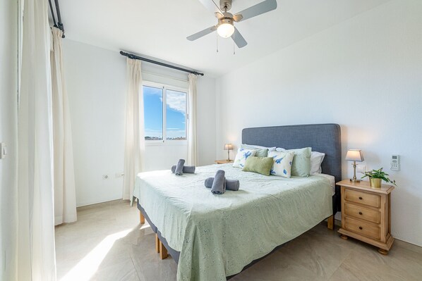 A bedroom with a bed, a nightstand, a ceiling fan, and a window with curtains.