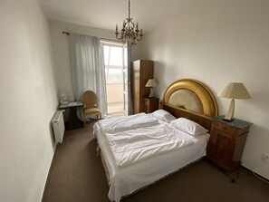 A hotel room with a bed, a desk, a chair, a wardrobe, and a chandelier.