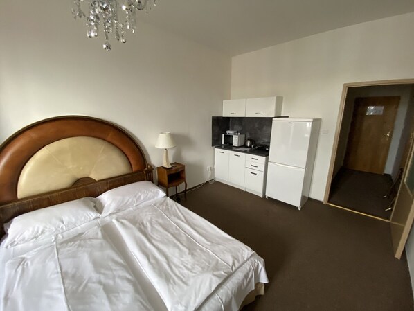 A hotel room with a bed, a kitchenette, and a door leading to another room.