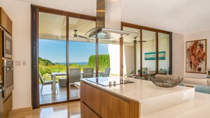 Una cucina moderna con una grande isola, porte scorrevoli in vetro che danno su un patio con vista sull'oceano.