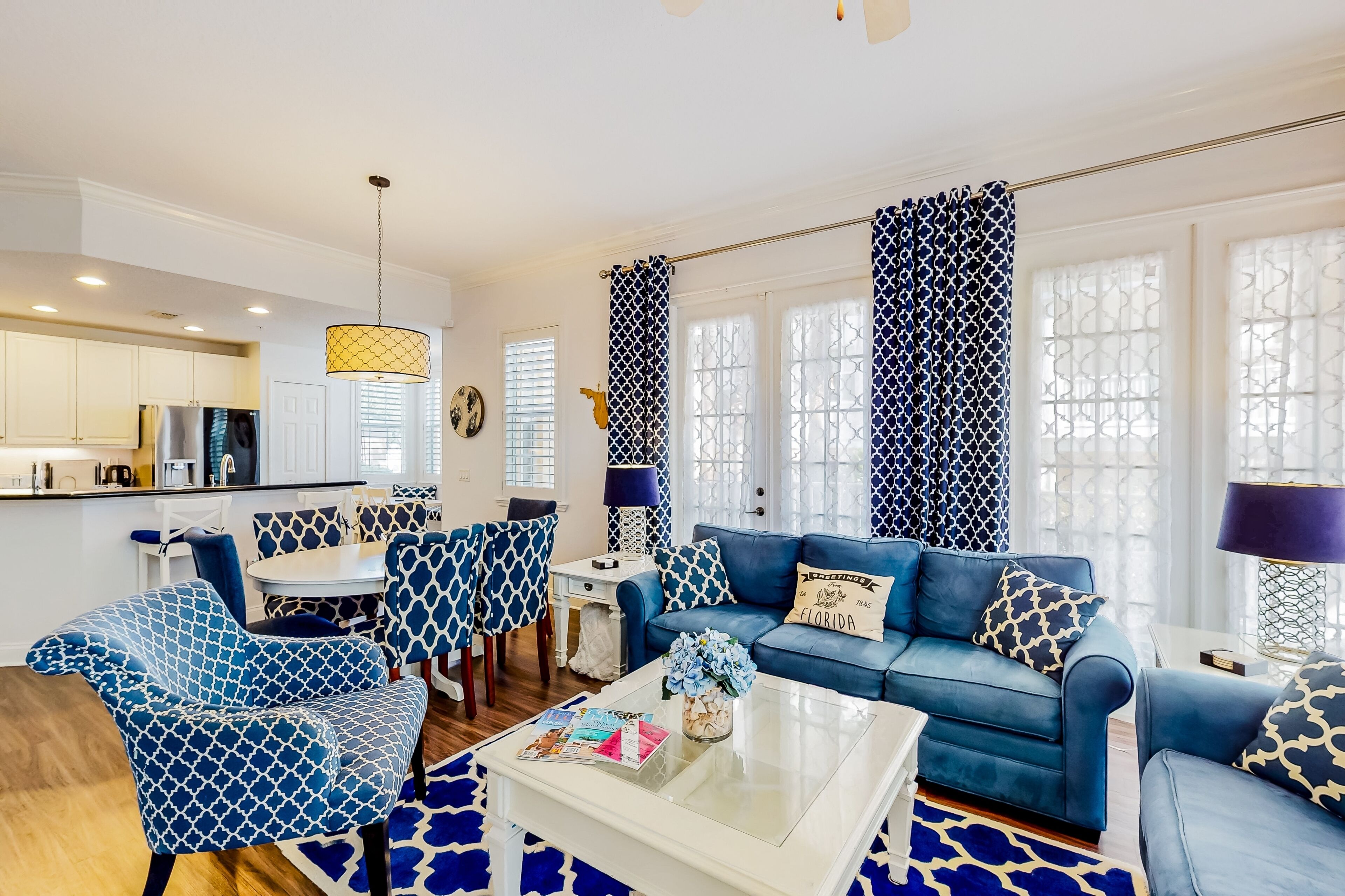 Un salon moderne avec un canapé bleu à motifs, des fauteuils assortis, une table basse et un coin repas.