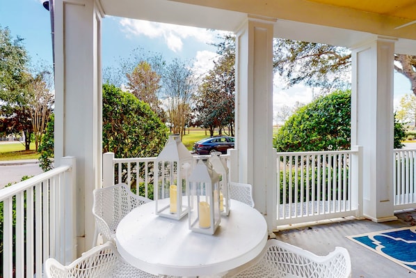 A covered outdoor area with a white table and chairs, white lanterns, and a view of a road and greenery. - Elevated Condo With Wraparound Porch at Reunion (Kissimmee)