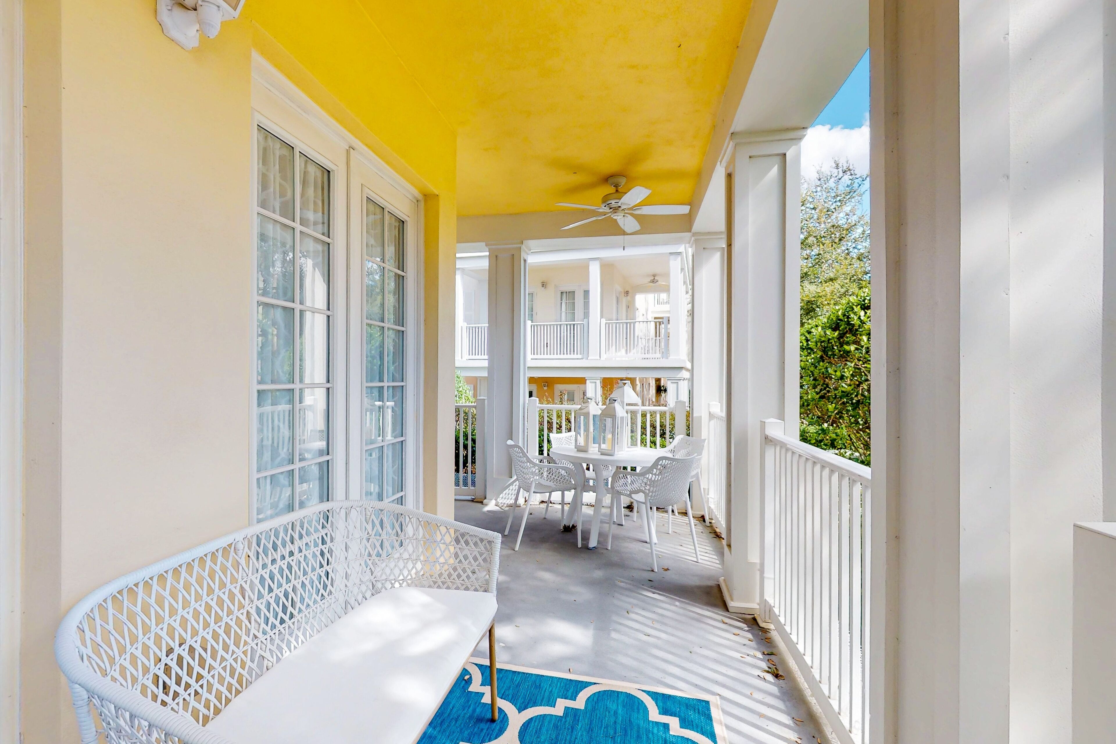 Une véranda avec un banc blanc, une table entourée de chaises et un ventilateur de plafond.