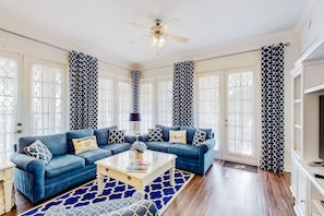 A living room with a blue sofa, a coffee table, and patterned curtains. - Elevated Condo With Wraparound Porch at Reunion (Kissimmee)