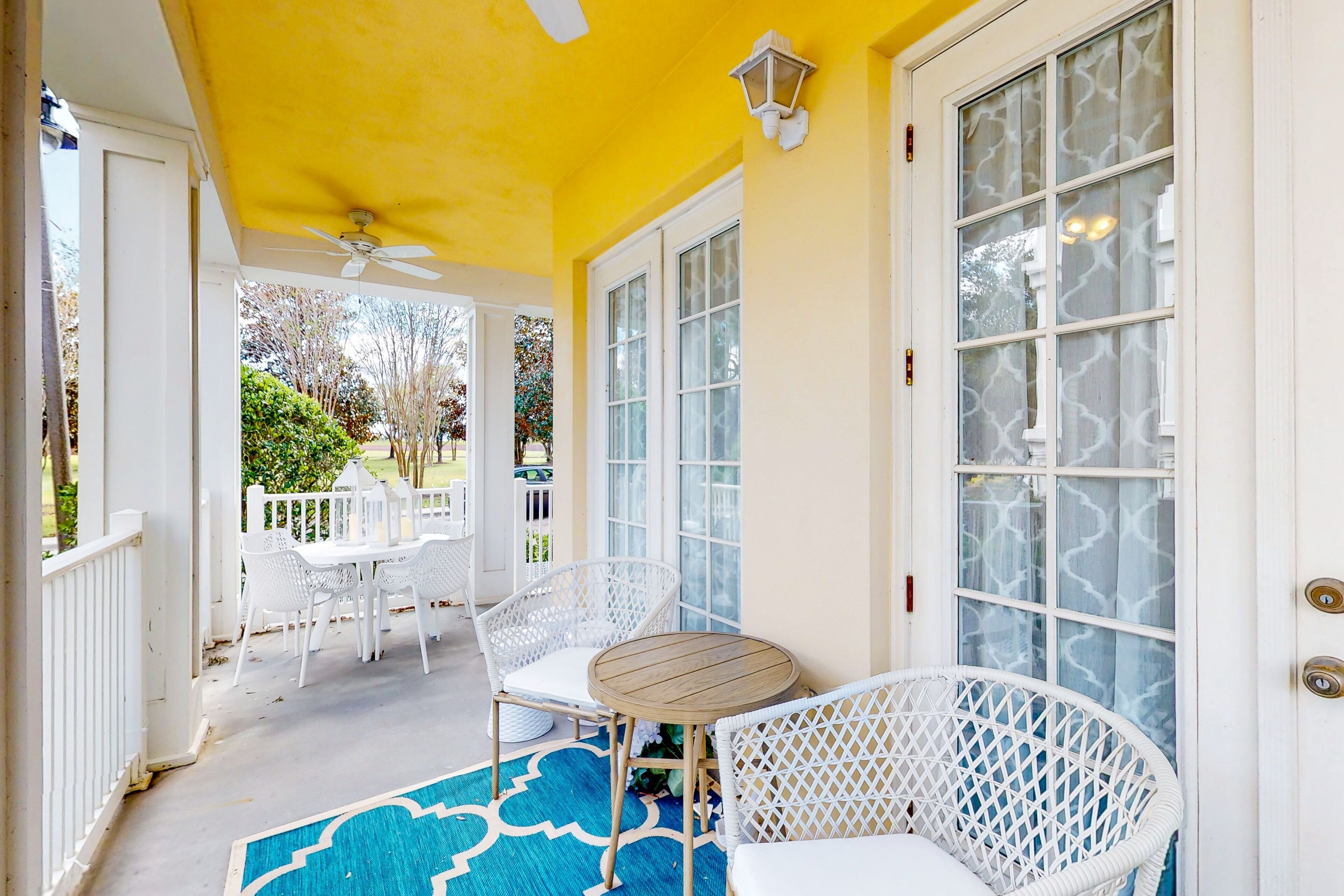 A covered porch with white wicker furniture, a round table, and a ceiling fan.