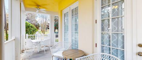 A covered porch with white wicker furniture, a round table, and a ceiling fan.