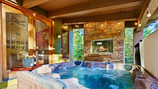 Een hottub met een achtergrond van een stenen muur, houten balken en een raam met uitzicht op groen.