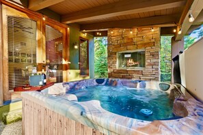 A hot tub with a stone wall backdrop, wooden beams, and a window overlooking greenery. - Near Lake and Downtown, Gameroom (McCall)