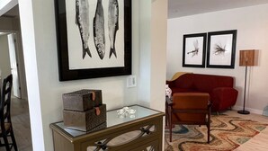 Un salon avec une table basse en verre, un canapé rouge et des œuvres d’art représentant des poissons, encadrées et accrochées au mur.