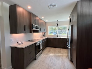 Una cocina moderna con armarios de madera oscura, un refrigerador de acero inoxidable, horno empotrado y un ventanal con vistas al exterior.