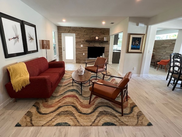 Una sala de estar con un sofá rojo, sillones de cuero marrón, un tapete estampado y una chimenea de piedra.