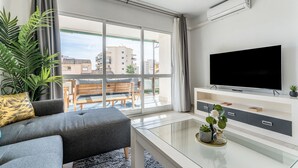 Ein modernes Wohnzimmer mit einer Couch, einem Couchtisch, einem Fernseher und einem Balkon mit Blick auf Gebäude.