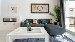 Ein modernes Wohnzimmer mit einem grauen Ecksofa, einem weißen Couchtisch und einem großen Fenster mit Vorhängen.