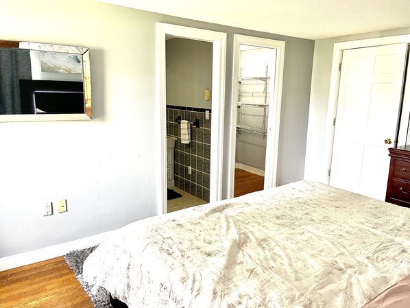 A bedroom with a bed, a wardrobe, a mirror, and a bathroom with a tiled wall and a towel rack. - Lovely & Spacious 2 Br, W/King/Queen beds 2 Bath. (Shrewsbury)