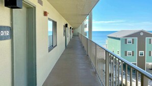 Un long couloir avec un balcon donnant sur une plage, orné d’un panneau indiquant le numéro « 312 » et d’une porte située sur la gauche.