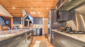 Une cuisine moderne dotée de plans de travail en granit, d’appareils électroménagers en acier inoxydable et de poutres en bois au plafond.