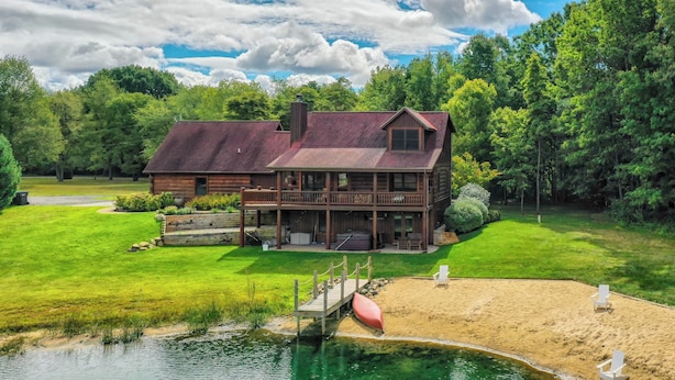 Une grande maison en bois dotée d’une terrasse, entourée d’une végétation luxuriante et bordée d’un lac.