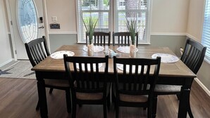 Une salle à manger avec une table en bois, quatre chaises, un lustre et de grandes fenêtres.