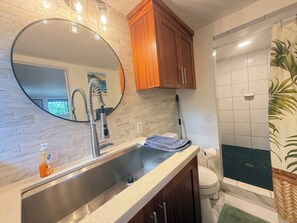 Un bagno con un lavandino moderno, uno specchio grande, mobili in legno e una zona doccia.