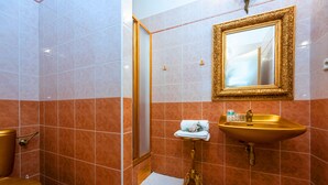Une salle de bain avec un lavabo doré, un miroir doté d’un cadre orné et un espace douche.