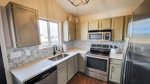 A modern kitchen with stainless steel appliances, patterned backsplash, and light-colored cabinetry.