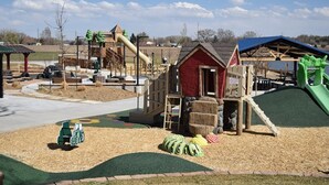 Ein Spielplatz mit Rutsche, Klettergerüsten und einem kleinen roten Gebäude.