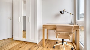 A room with a wooden desk, a leather chair, a desk lamp, and a white wardrobe.
