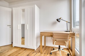 Una habitación con un escritorio de madera, un sillón de cuero, una lámpara de escritorio y un armario blanco.