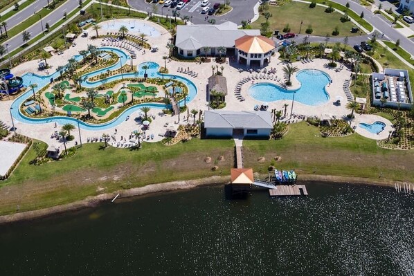 An aerial view of a resort with multiple swimming pools, a water slide, and a dock.