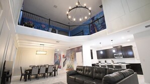 A spacious living area with a high ceiling, a dining area with a chandelier, and a kitchen with dark cabinets. - 5BR/5BA Game/Pool Villa 9 Miles to Disney (Kissimmee)