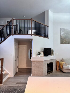 A two-story home with a staircase, a fireplace, a television, and a painting on the wall.