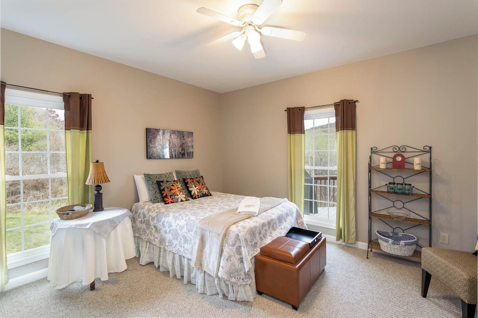 A bedroom with a bed, bedside tables, a nightstand, a window with curtains, a ceiling fan, and a shelf with items.