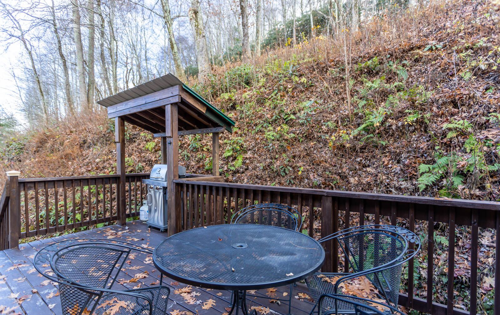 An outdoor patio with a round metal table and chairs, a barbecue grill, and a wooden pergola.