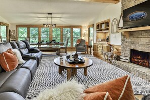 A spacious living room with a fireplace, leather sofa, and a television displaying 'Blue Sky Cabin Rentals.'