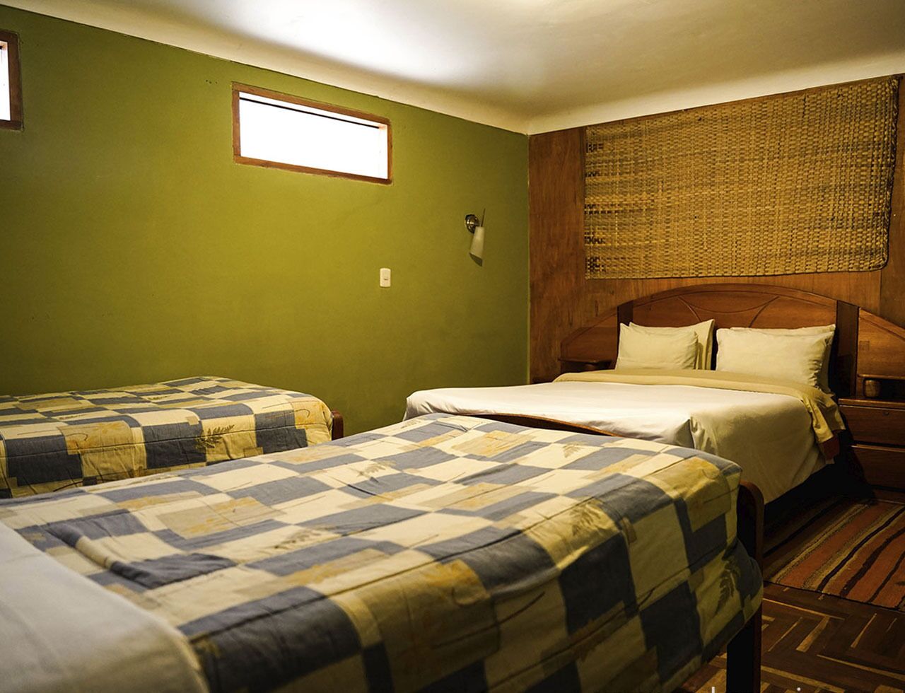 A room with two beds, a wooden headboard, a small window, and a woven mat on the wall.