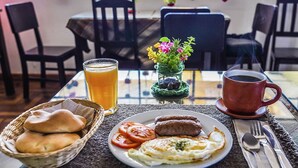 Ein Esstisch mit Brot, Eiern, Tomaten, einem Glas Orangensaft, einer Tasse Kaffee und einer kleinen Vase mit Blumen.
