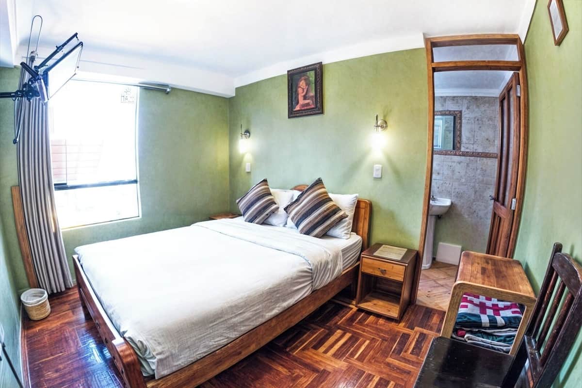 A bedroom with a wooden bed, a bedside table, a chair, and a window with curtains.